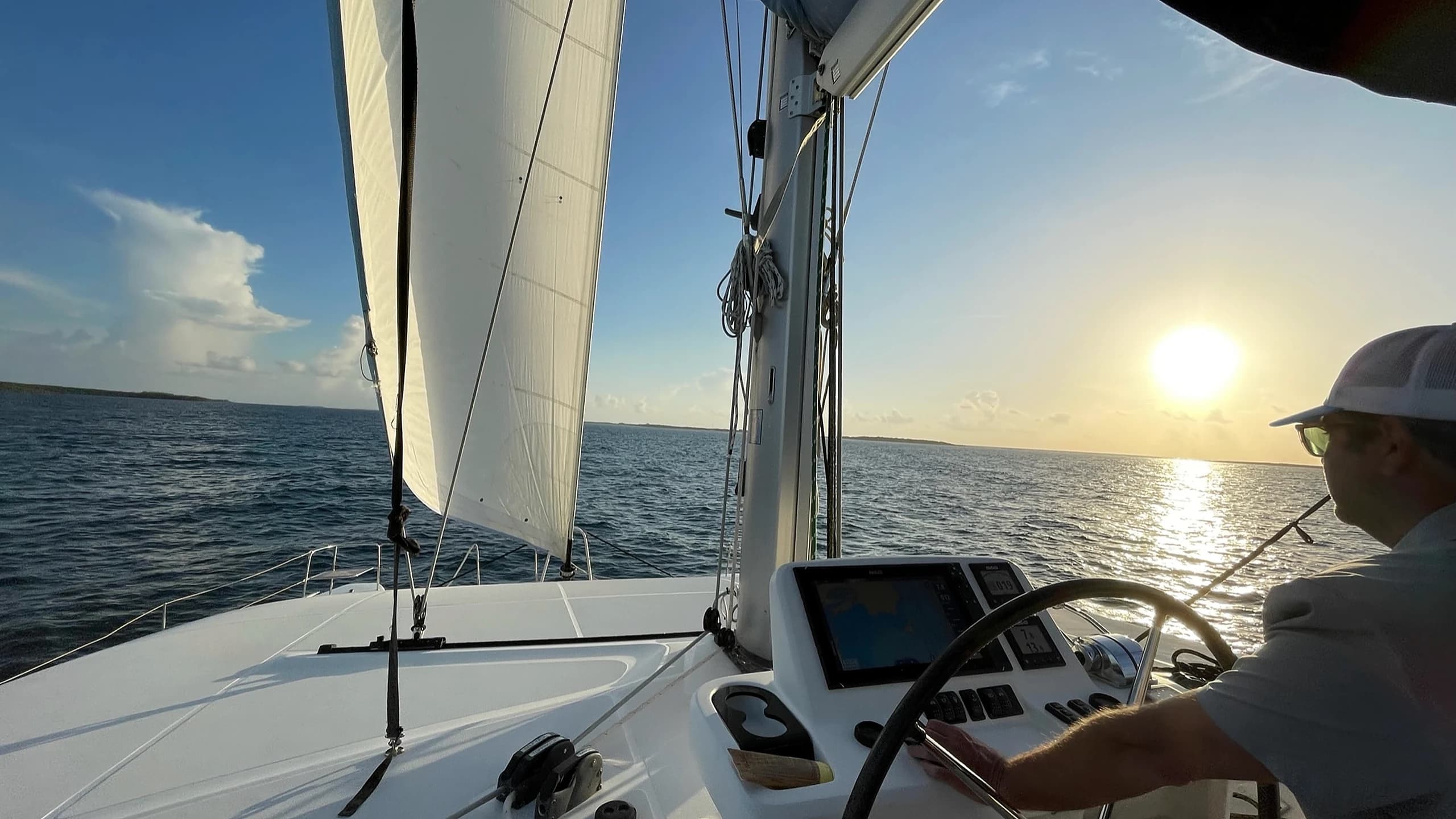 A sailor at the helm of a catamaran at sunset, Sea of Abaco