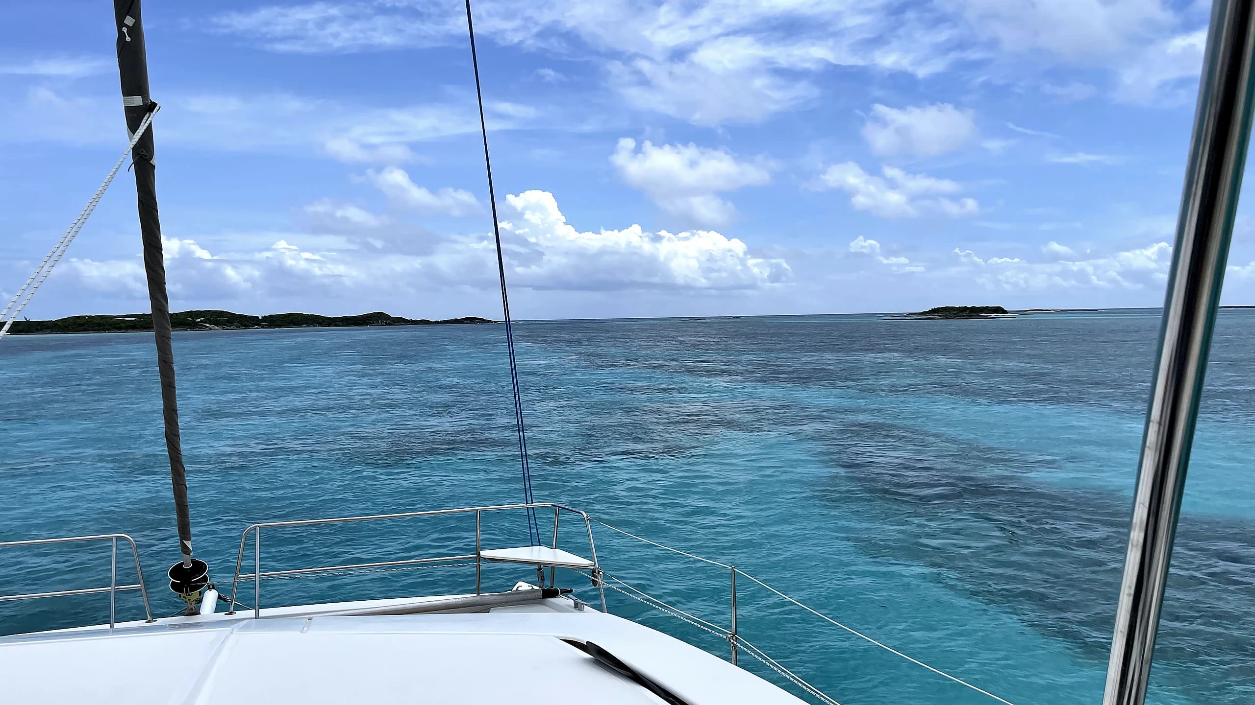 A catamaran approaches a turquoise Exumas anchorage with low cays on the horizon